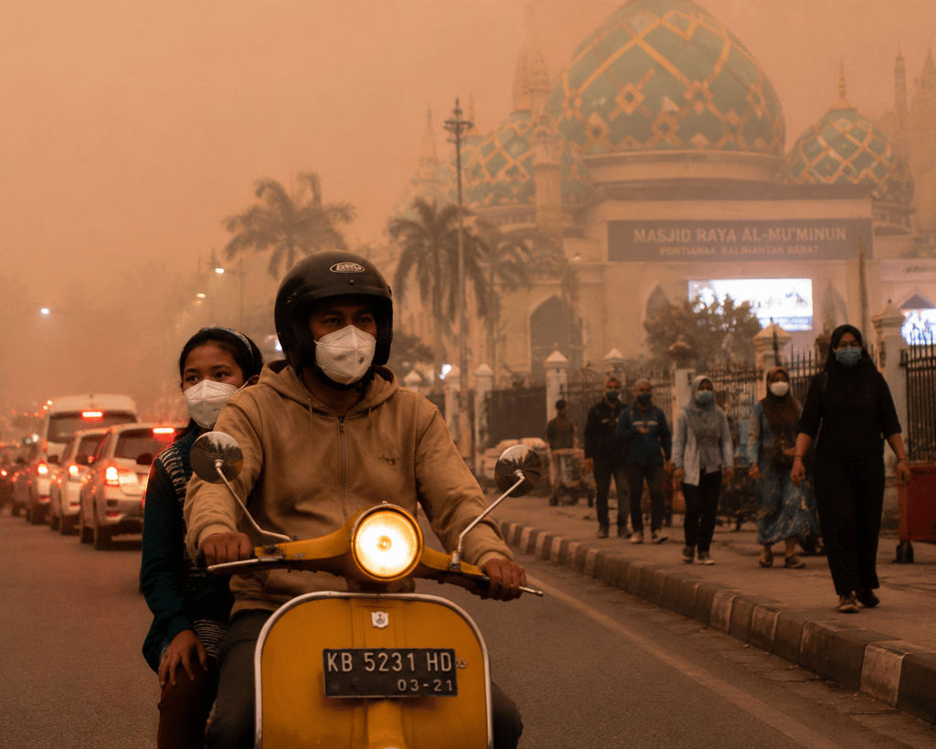 Pengendara sepeda motor dan pejalan kaki menggunakan masker N95 di jalanan Pontianak di bawah kabut asap karhutla pekat El Nino.